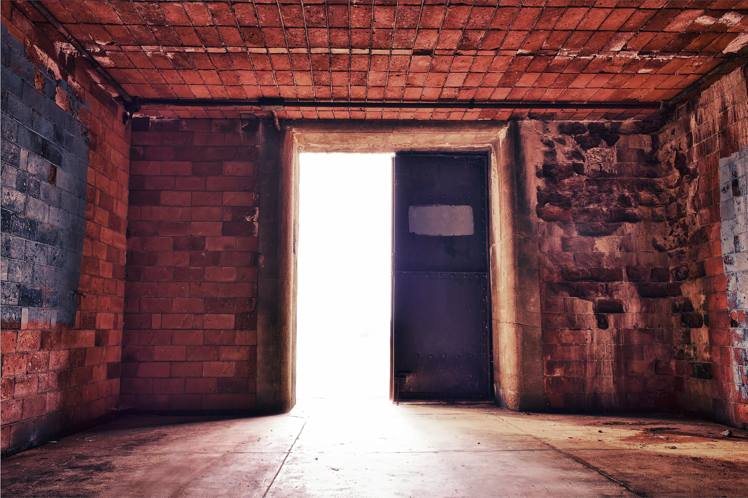 An eerie backlit door to an abandoned and weathered brick and concrete room.