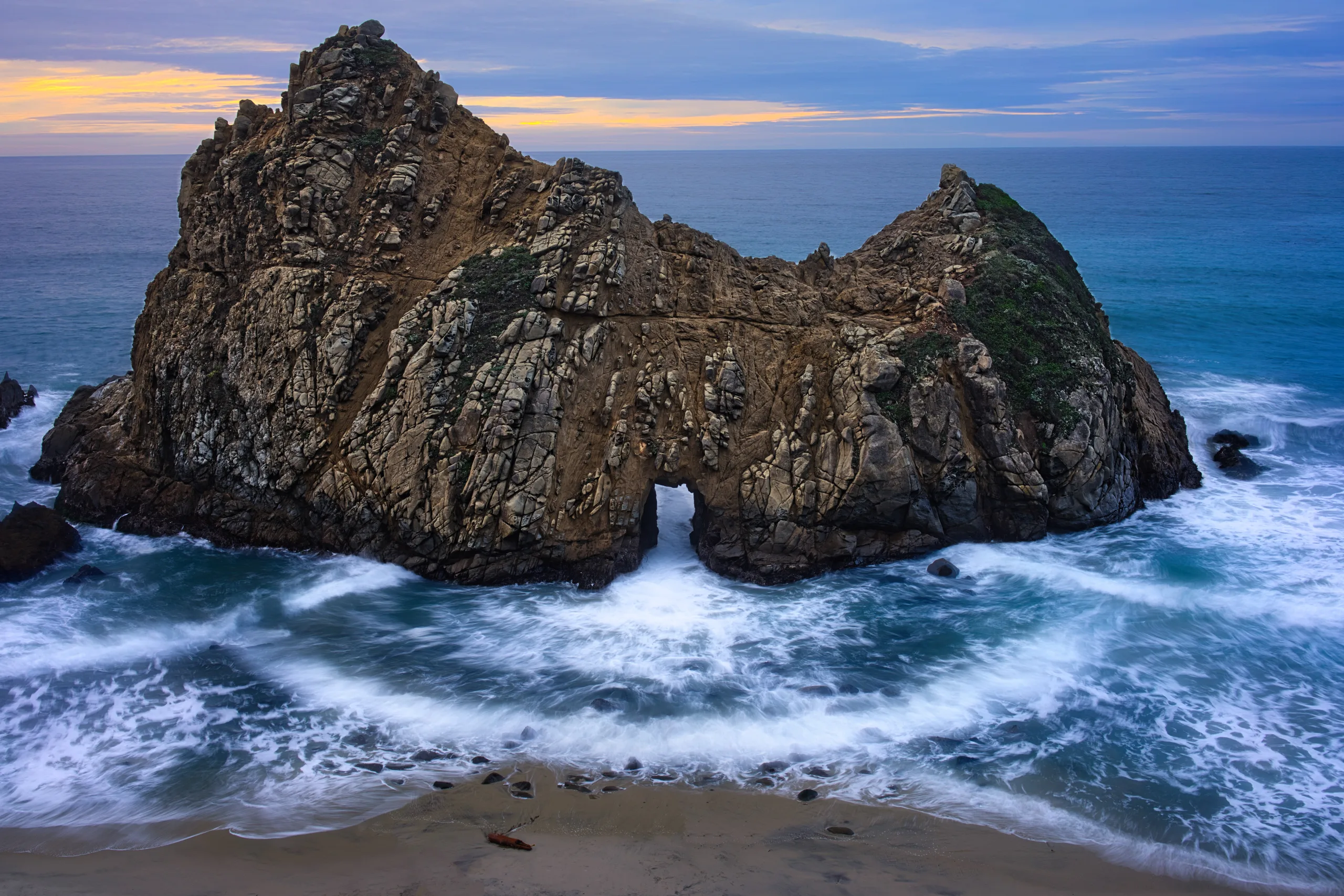 Aerial view of a cool winter sunset over Pfeiffer Beach's keyhole rock with gentle waves.